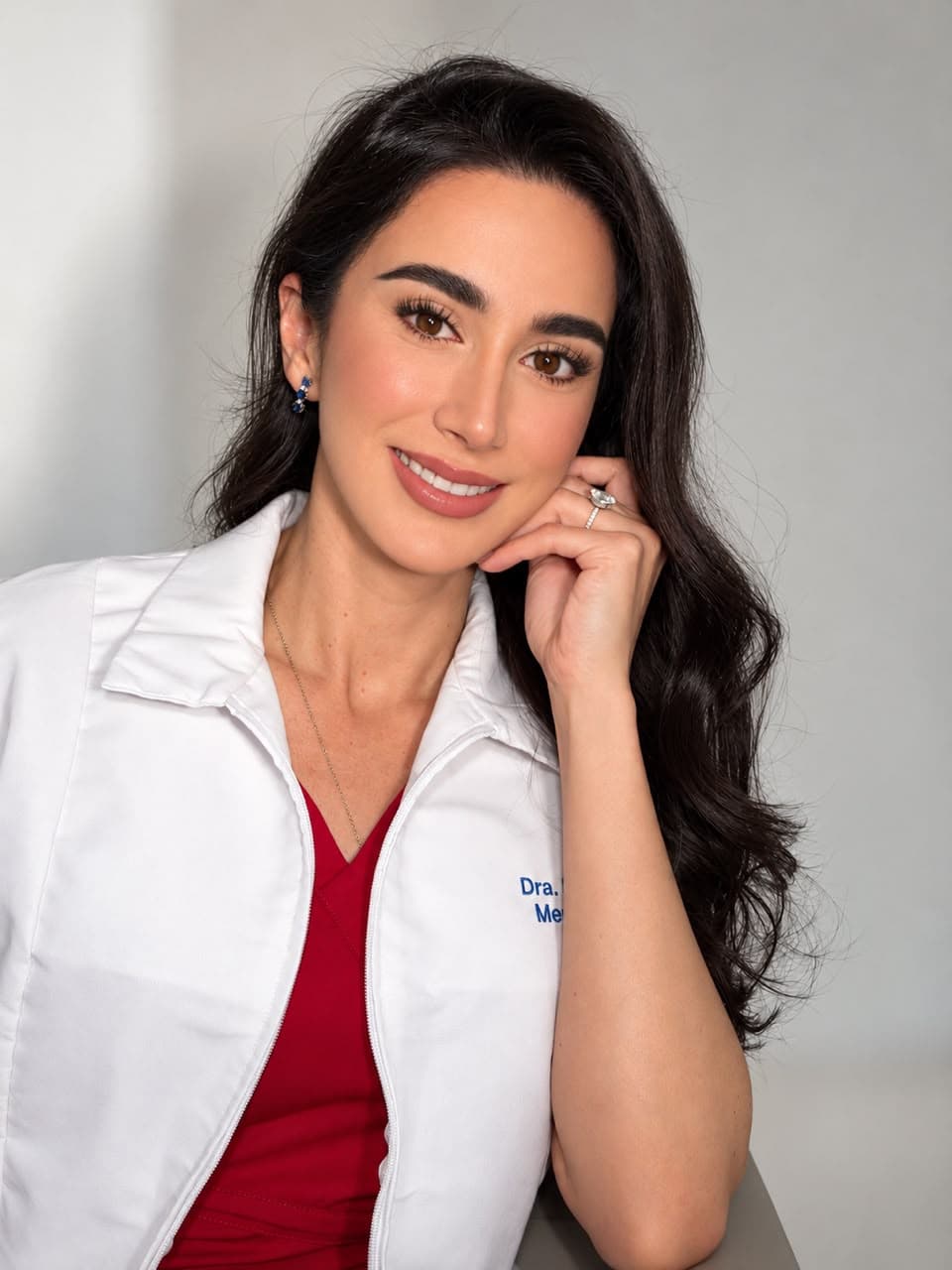 Dr. Marisol Gomez Martinez in a white medical coat, smiling with her hand beside her face.